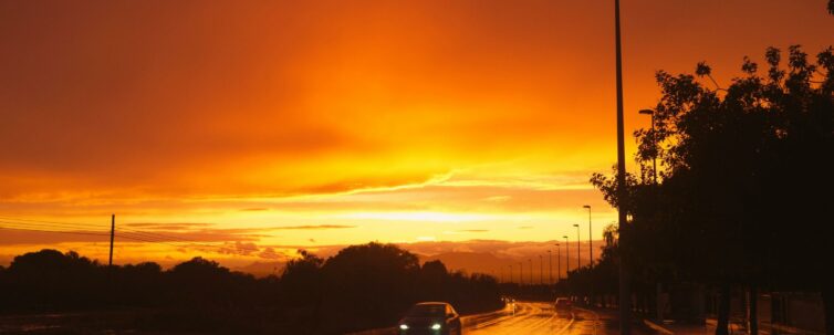 wet road with a car with headlight on and the sun is setting