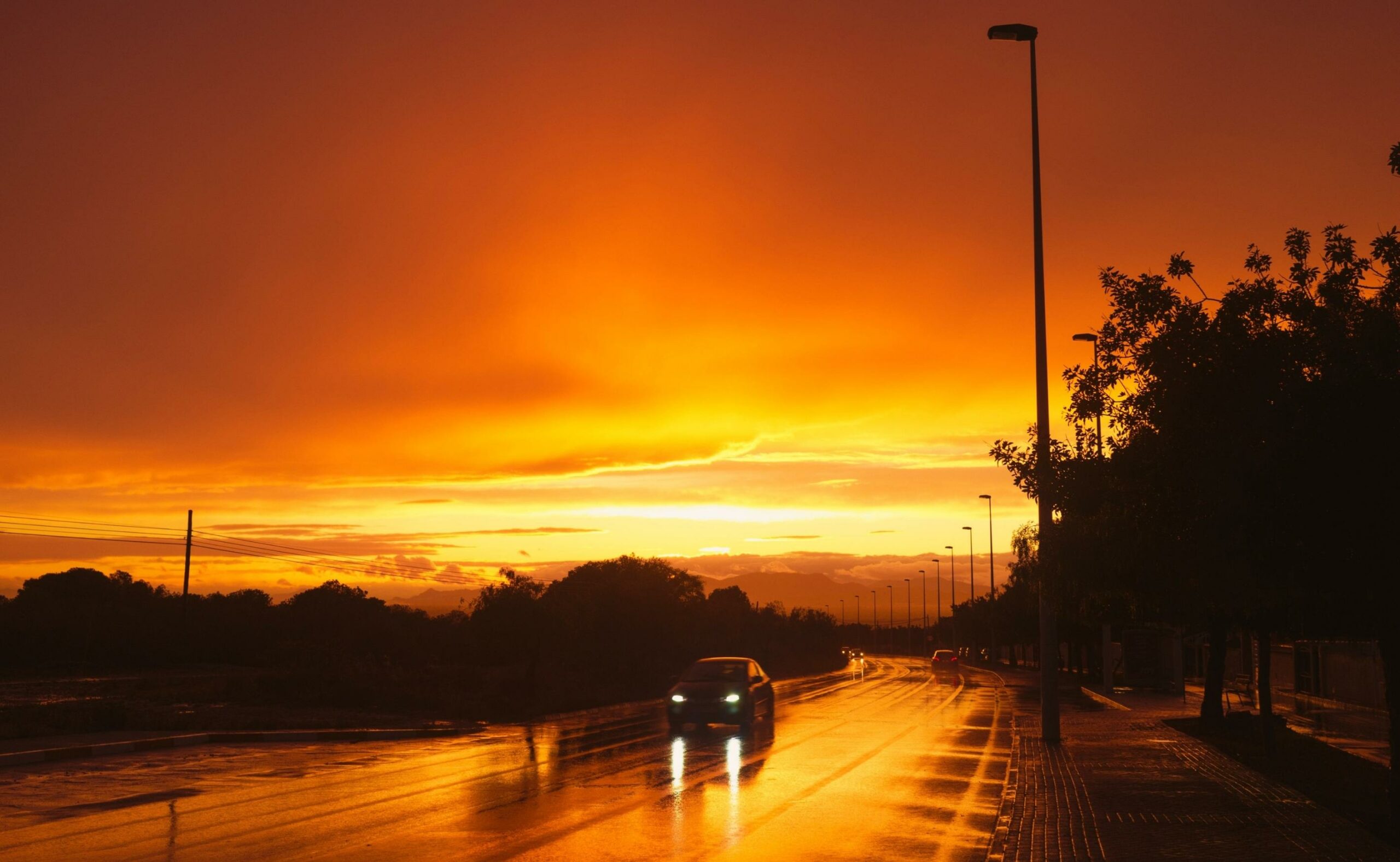 wet road with a car with headlight on and the sun is setting