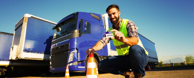 New truck driver showing his license with trucks behind him