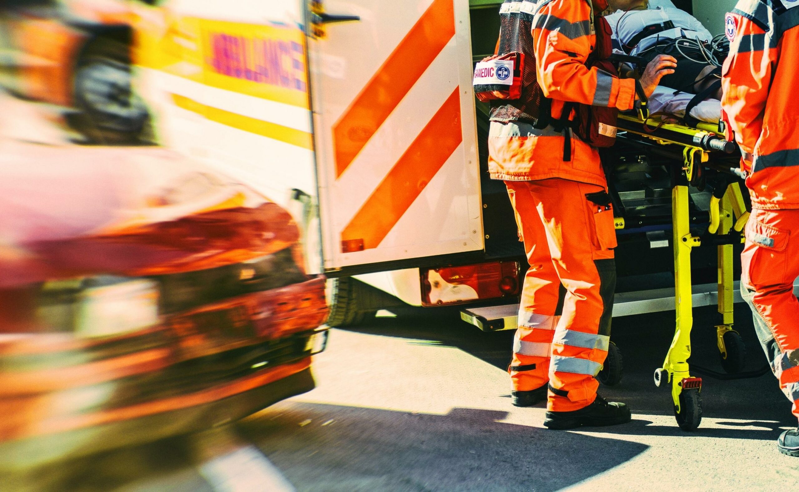 Rescuers putting man in stretcher inside an ambulance. Wrecked car beside the ambulance