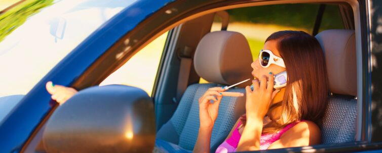 a teen girl applies makeup and talks on her cellphone while driving