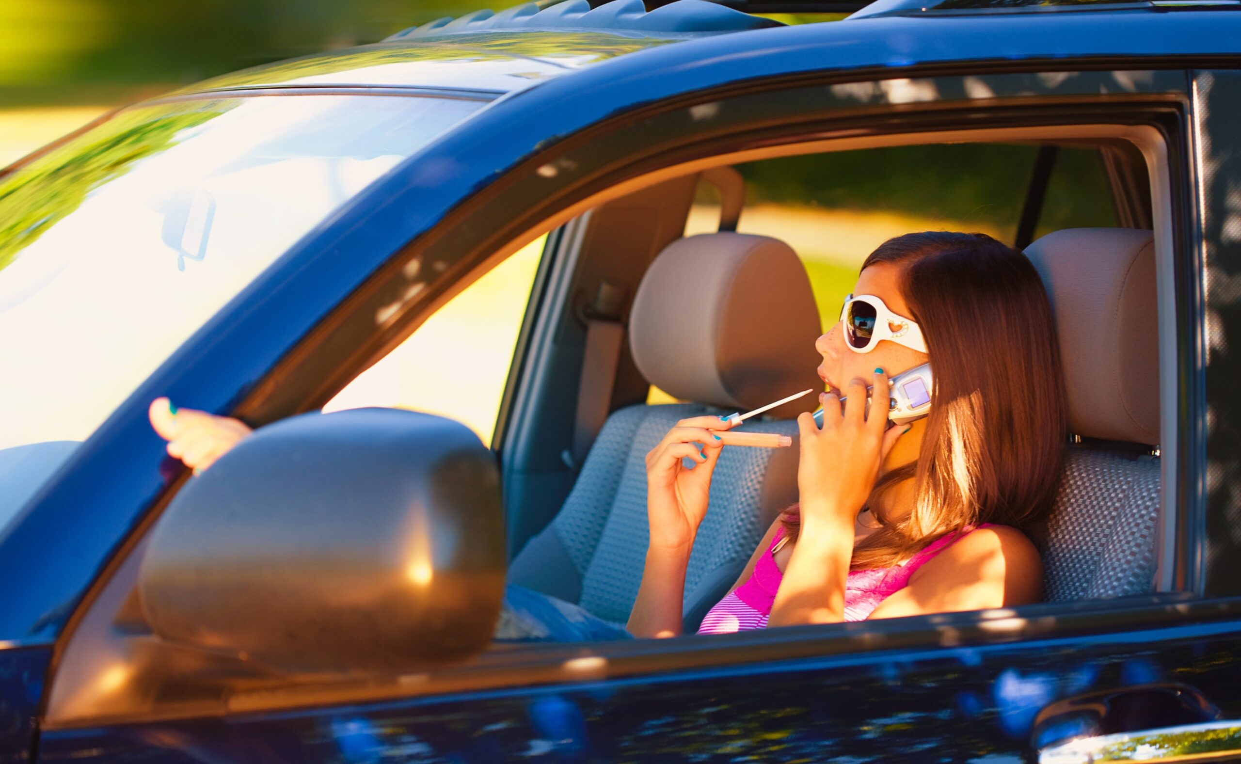 a teen girl applies makeup and talks on her cellphone while driving