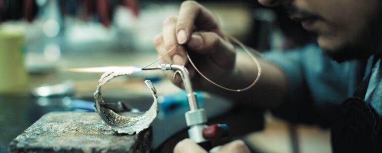 Close up shot of jeweler hand making jewelry with silver and gold using bunsen burner in jewelry manufacture workshop