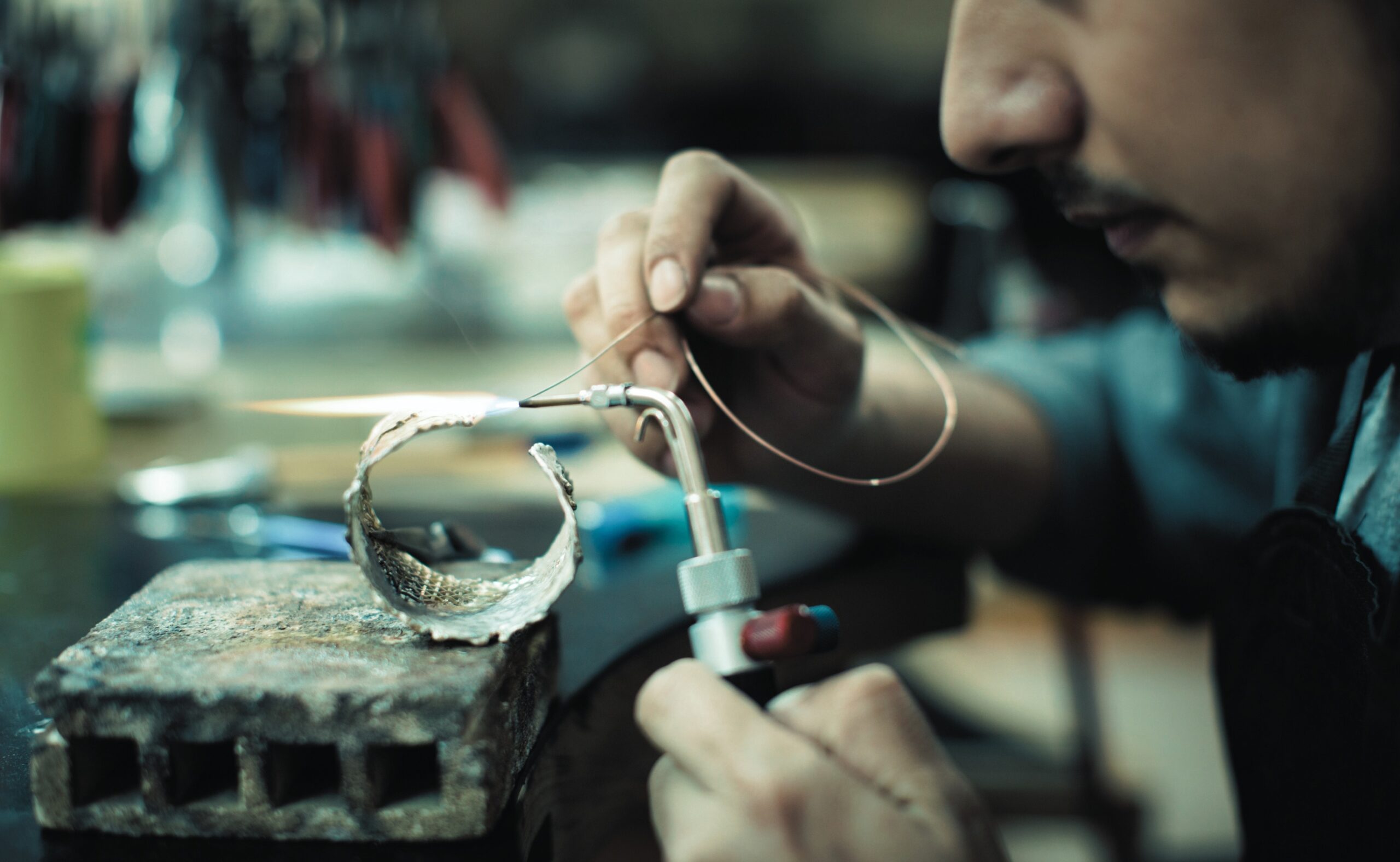 Close up shot of jeweler hand making jewelry with silver and gold using bunsen burner in jewelry manufacture workshop