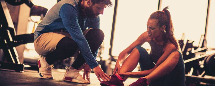 Sportswoman with personal trainer in gym having leg injury