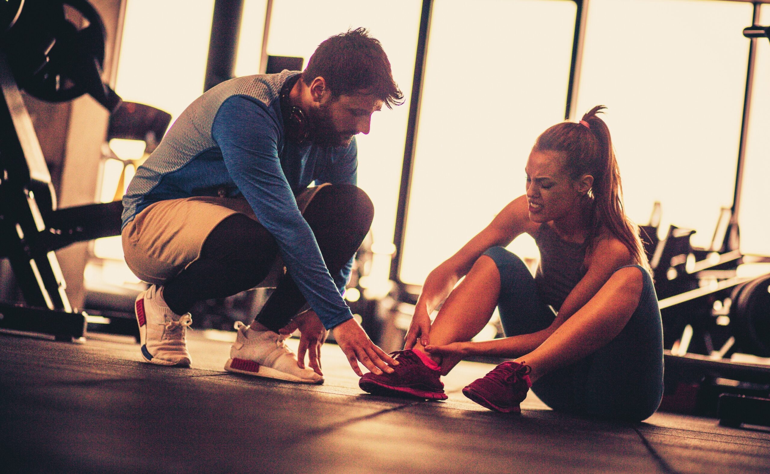 Sportswoman with personal trainer in gym having leg injury