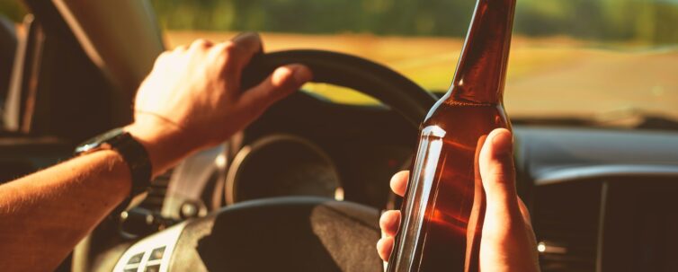 Man driving a car holding a a bottle of beer