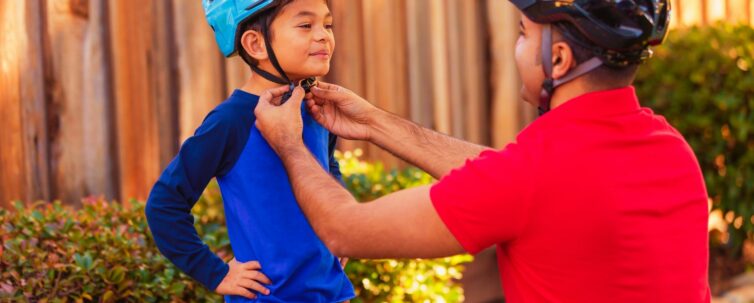 Father helping his son put on athletic sports helmet for bicycle riding