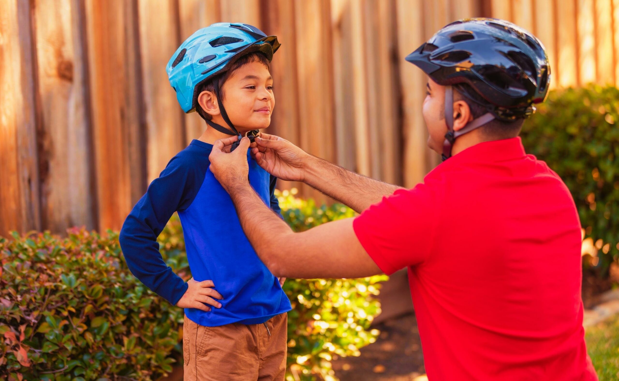 Father helping his son put on athletic sports helmet for bicycle riding