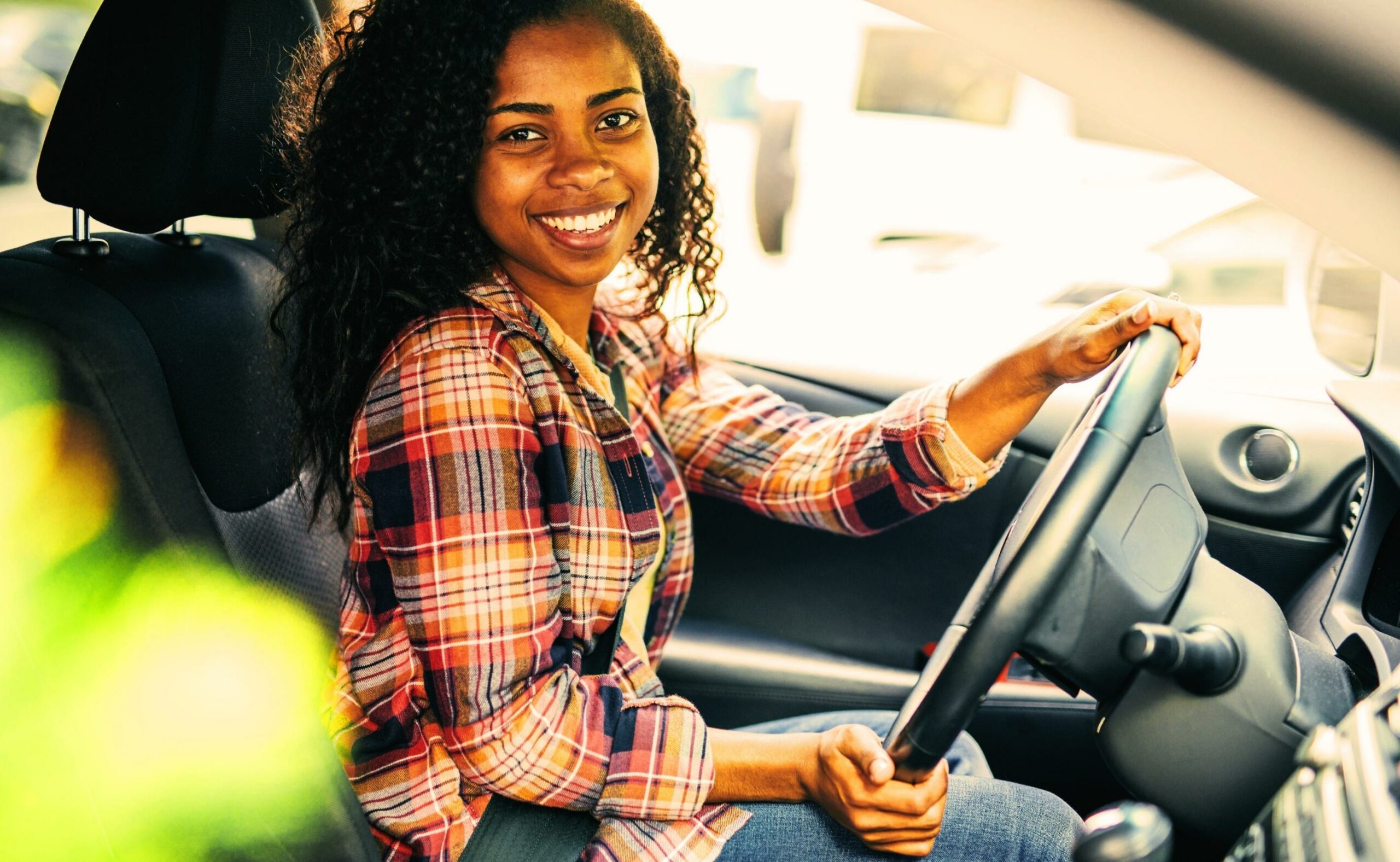 Millennial on driver side of car, holding the steering wheel smiling after the camera