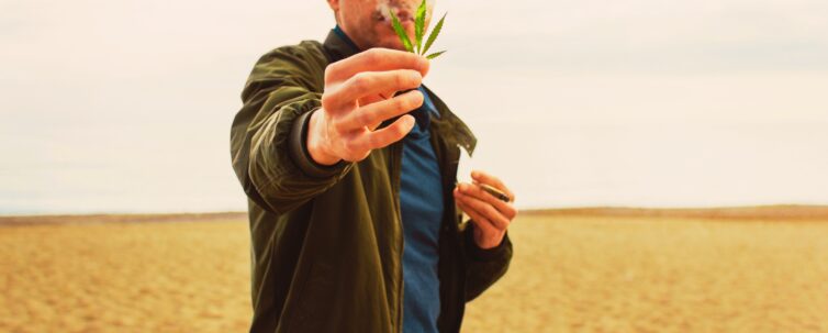 Young man holding marijuana leaf and smoking a cannabis joint on the beach
