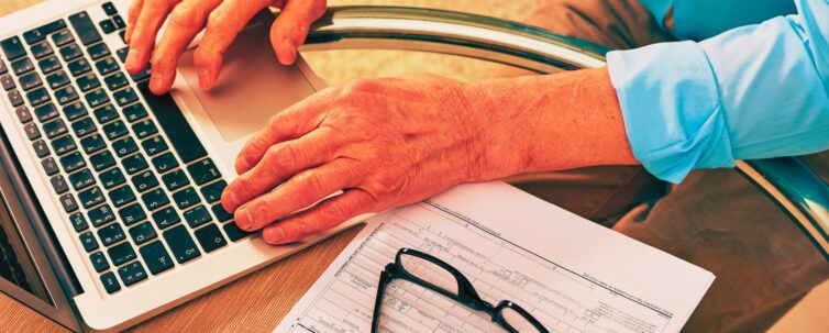 senior man sitting at glassy table and using laptop while filing a claim