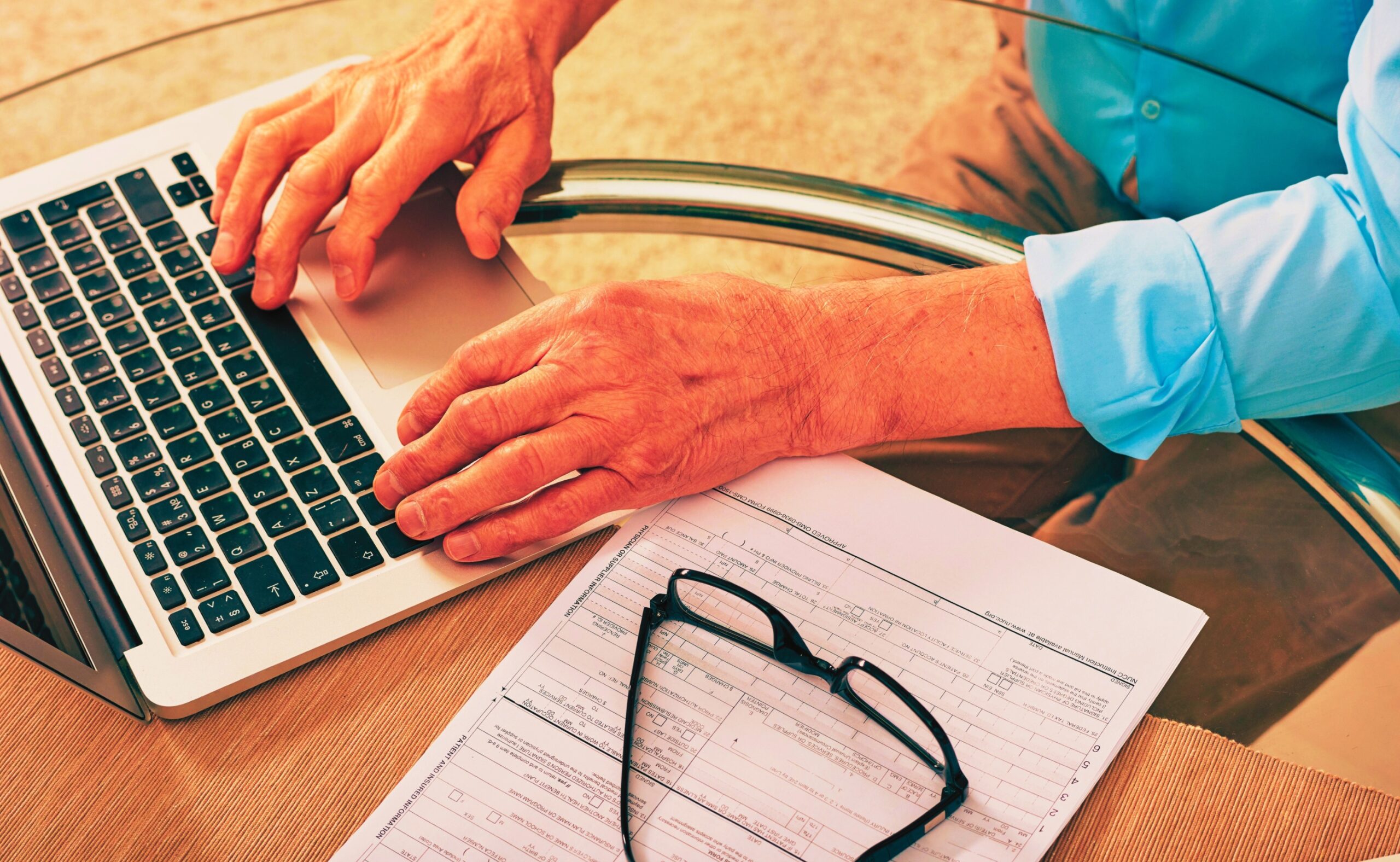 senior man sitting at glassy table and using laptop while filing a claim