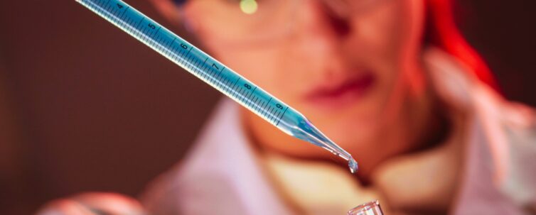 woman using pipette to put drops of blue liquid into test tube in a lab