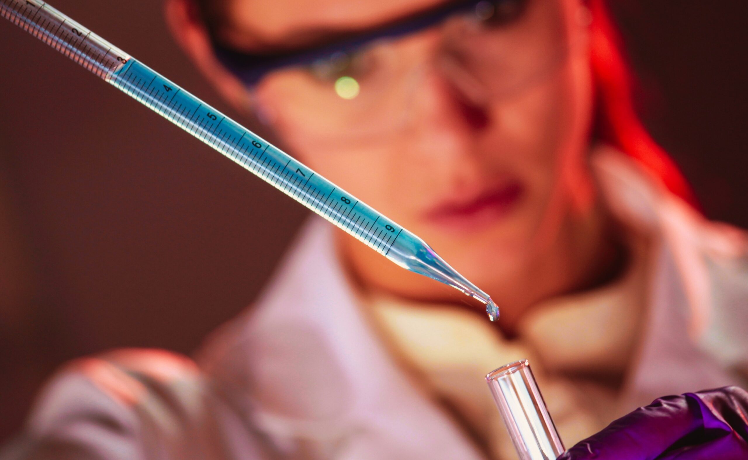 woman using pipette to put drops of blue liquid into test tube in a lab