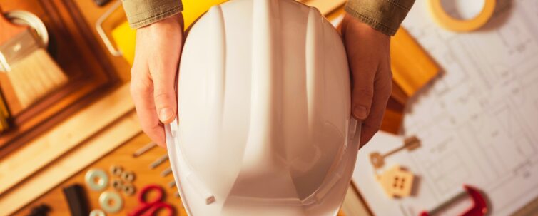 Hands holding protective safety helmet against a work table with hardware and construction tools