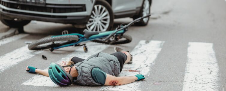 Scene of a road accident with injured cyclist lying on the pedestrian crossing near the broken bicycle and car