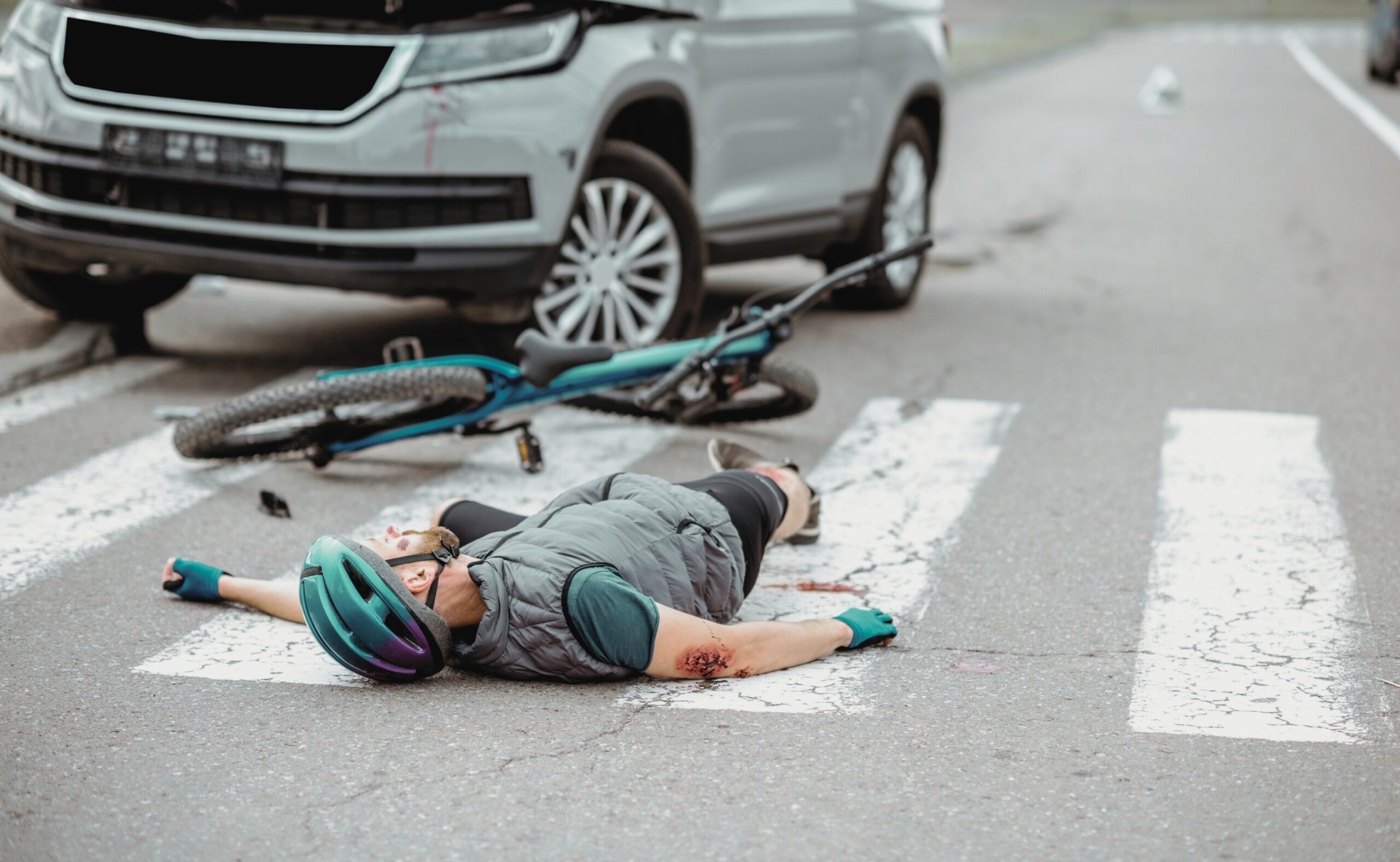Scene of a road accident with injured cyclist lying on the pedestrian crossing near the broken bicycle and car