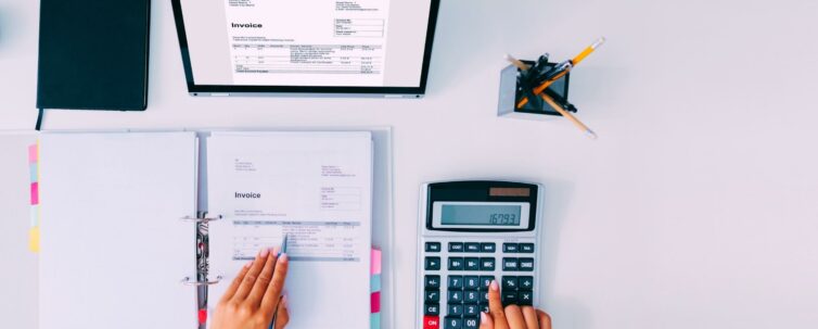 accountant computing tax/invoice using calculator with ledger and laptop on desk