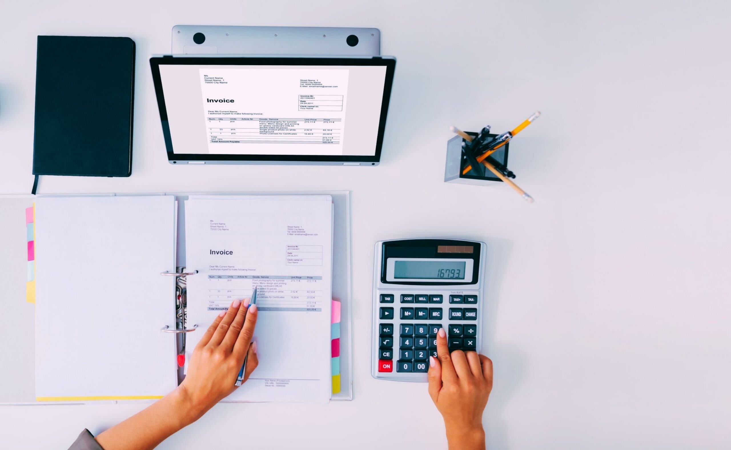 accountant computing tax/invoice using calculator with ledger and laptop on desk