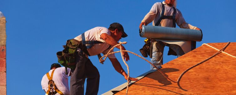 roofers on an 8-12 pitch roof laying under-layment before installing roof tile
