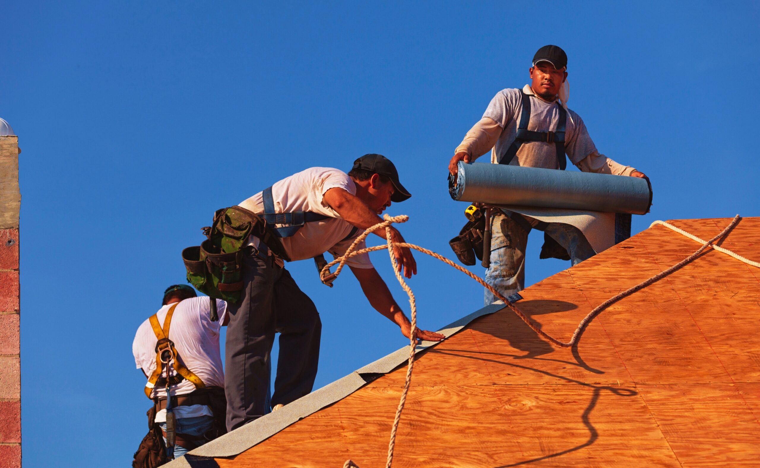 roofers on an 8-12 pitch roof laying under-layment before installing roof tile