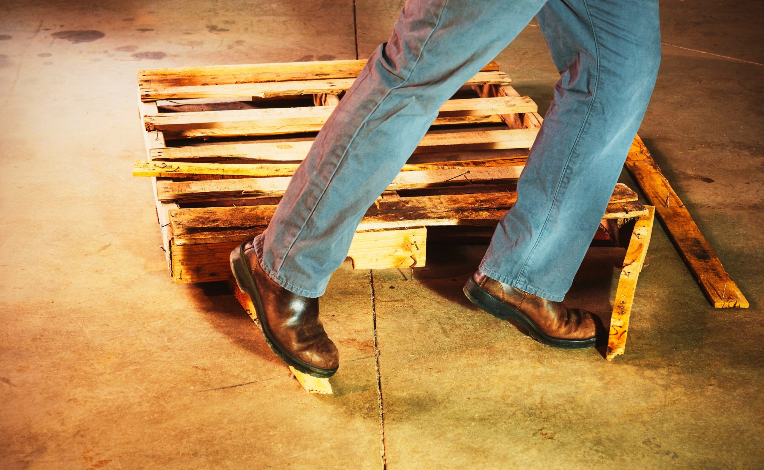 warehouse safety. a person trips of a damaged pallet in a warehouse.