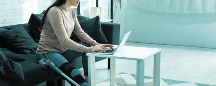 beautiful woman with broken leg having online consultation with doctor on laptop at home