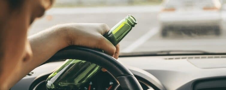 Drunk young man driving a car with a bottle of beer
